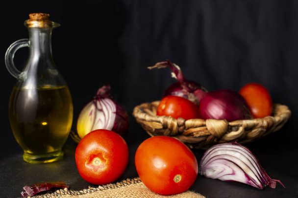 新鮮な野菜、サラダやスペインのガスパチョの成分のカラフルな静物画。赤いトマト梨、紫色のタマネギとオリーブオイルのボトル。水平方向の眺め。黒の背景. - 写真・画像