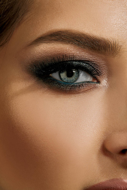 Face of a lady with luxury makeup and perfect skin. Gray eyeshadow, long eyelashes, matte beige lips, brown eyebrows. Professional maquillage. Close up - Foto, Bild