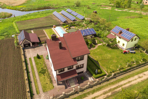 Luchtfoto van een particulier huis in de zomer met blauwe zonnepanelen op dak en in de tuin. - Foto, afbeelding