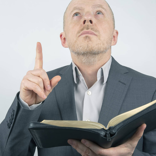 Ο άντρας με το κοστούμι διαβάζει τη Βίβλο. Ένας άντρας σήκωσε το δάχτυλό του. - Φωτογραφία, εικόνα