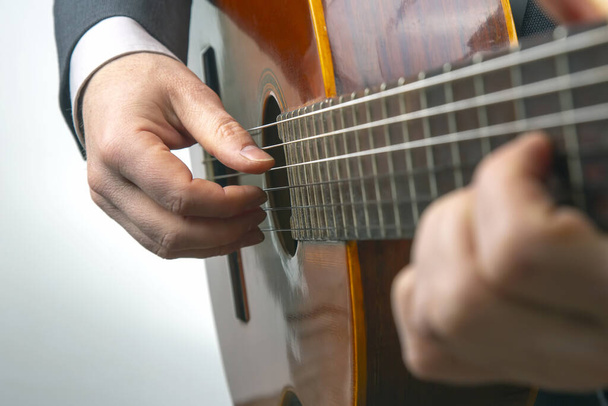 Человек играет на классической гитаре на белом фоне. музыкальное творчество. струнный музыкальный инструмент - Фото, изображение