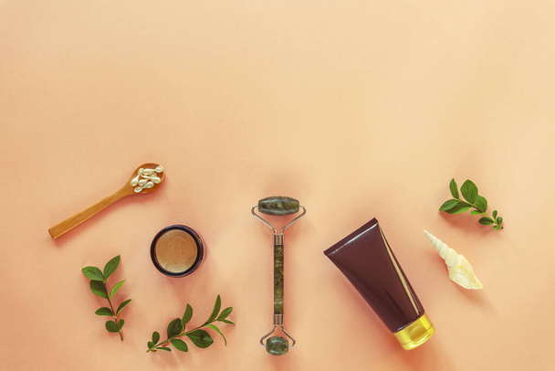 Flat lay of beauty products: facial roller, cream jar, capsules with serum and body lotion on coral background, top view, copy space - Photo, Image