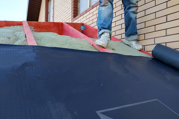 El trabajador desenrolla un rollo de película aislante y lo cubre con un tejado.2020
 - Foto, Imagen