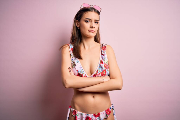 Junge schöne Frau im Urlaub mit Bikini und Sonnenbrille über rosa Hintergrund skeptisch und nervös, missbilligenden Gesichtsausdruck mit verschränkten Armen. Negative Person. - Foto, Bild