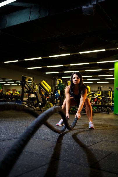 The girl in the gym does an exercise with ropes in her hands. - Foto, Bild