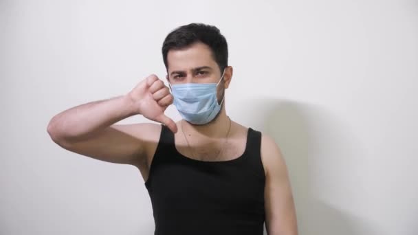 Caucasian man puts on his medical mask looks into camera and one thumb down Covid19 Coronavirus - Filmmaterial, Video