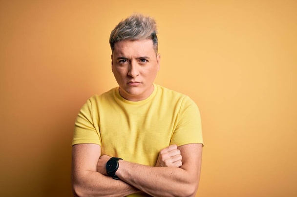 Young handsome modern man wearing yellow shirt over yellow isolated background skeptic and nervous, disapproving expression on face with crossed arms. Negative person. - Zdjęcie, obraz