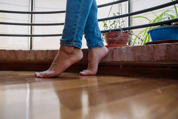 barefoot of a caucasian girl with blue jeans, on tiptoe, in wooden floor, with beautiful plants - Photo, Image