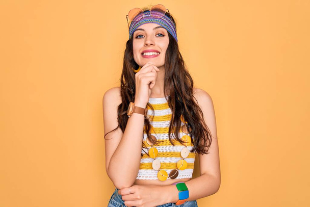 Jonge mooie hippie vrouw met blauwe ogen dragen accessoires en zonnebril kijken vol vertrouwen naar de camera glimlachend met gekruiste armen en hand geheven op kin. Positief denken. - Foto, afbeelding