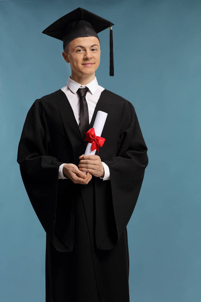 Male graduate student holding a diploma isolated on blue background - Photo, Image