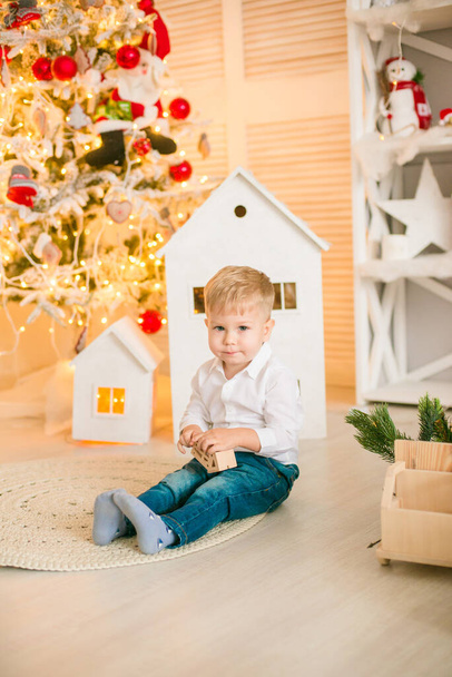 Cute little boy with blond hair plays with  toys in a bright room decorated with Christmas garlands near the Christmas tree. Happy childhood. Christmas mood - Foto, imagen