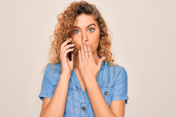 Young beautiful blonde woman with blue eyes having conversation talking on the smartphone cover mouth with hand shocked with shame for mistake, expression of fear, scared in silence, secret concept - Photo, Image
