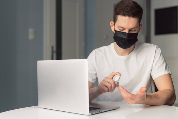 Man working from home during coronavirus quarantine, wearing black protective mask. Working from home. Cleaning her hands with sanitizer gel. Close up photo of sanitizer gel - Foto, Imagen