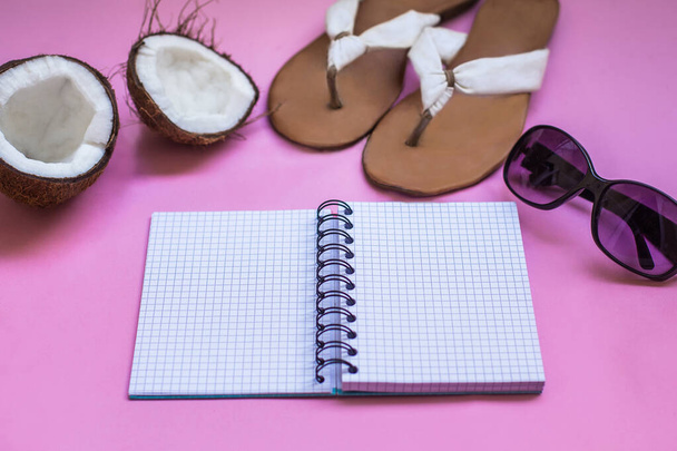 Urlaubs- und Reisekonzept. Reisekoffer. Notizbuch mit Sommerschuhen, Sonnenbrille, exotischer Kokosnuss auf rosa Hintergrund.  - Foto, Bild