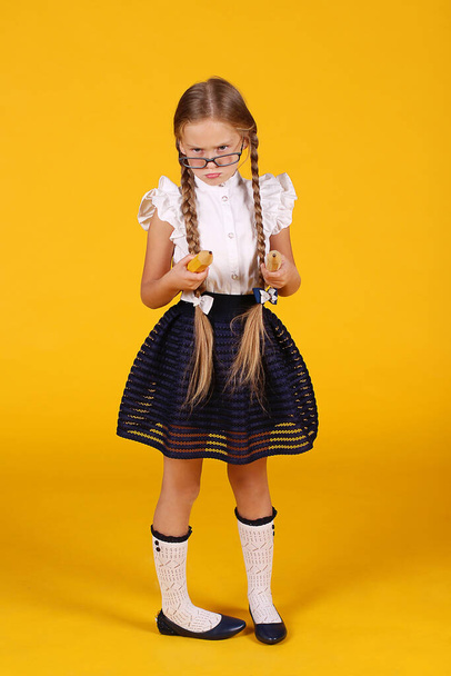 Chica creativa fresca de primer grado con trenzas largas en un uniforme escolar y gafas. En manos de lápices grandes. Fondo amarillo. Papelería
. - Foto, Imagen
