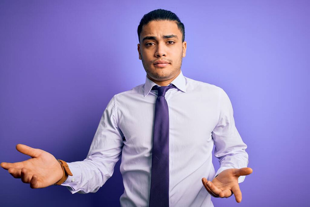 Nuori brasilialainen liikemies yllään tyylikäs solmio seisoo eristetty violetti tausta tietämätön ja sekoittaa avosylin, ei aavistustakaan käsite
. - Valokuva, kuva