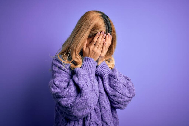Giovane bella donna bionda indossa casual maglione dolcevita su sfondo viola con espressione triste che copre il viso con le mani mentre piange. Concetto di depressione
. - Foto, immagini
