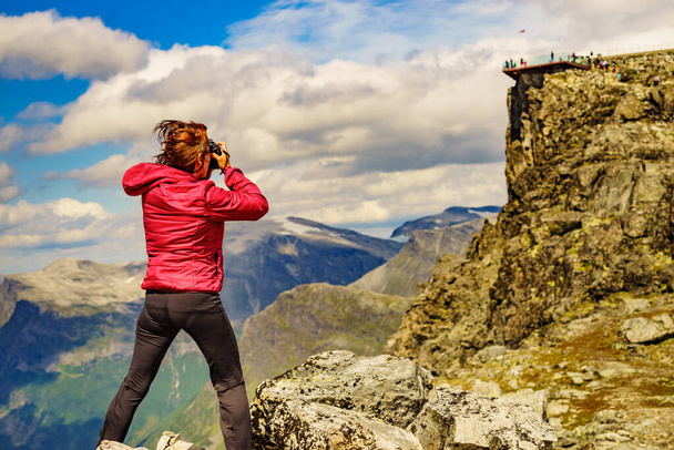 Tourism vacation and travel picture. Female tourist taking photo with camera, enjoying mountains landscape at windy day. Dalsnibba Plateau viewpoint in the distance, Norway . - Fotoğraf, Görsel