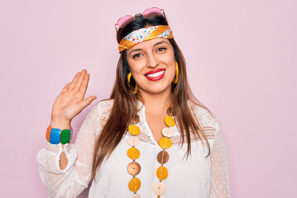 Junge hispanische Hippie-Frau trägt Mode-Boho-Stil und Sonnenbrille über rosa Hintergrund Verzicht auf Hallo glücklich und lächelnd, freundliche Willkommensgeste - Foto, Bild