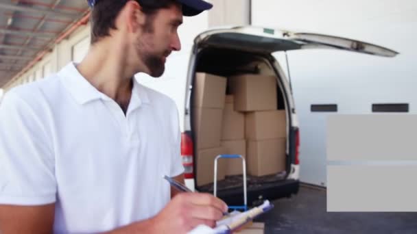 Animation of the words Free Delivery written in white on orange and grey banners, a male van driver standing next to his van full of stacked up boxes and parcels by a warehouse giving a thumbs up and smiling to camera. - Materiaali, video