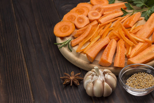 Raw chopped carrots on cutting board. Garlic and mustard seeds on table.  Natural  Close up. Dark wooden background. Copy space - Foto, imagen