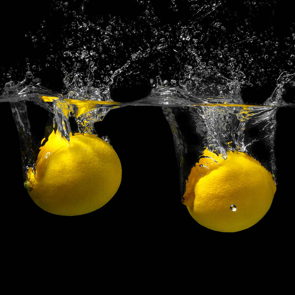 レモンは黒い背景に水に沈む。水飛沫のついた柑橘類 - 写真・画像