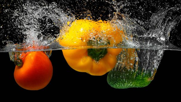 Fresh vegetables splashing in water on black background.whole fresh cucumber, radish, tomato in water with spray. - Photo, Image