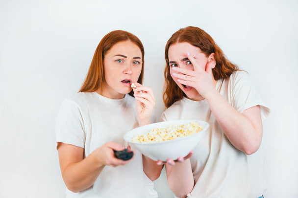 two redheaded scared women look frightened one with remote control another with popcorn standing on isolated white backgroung, leisure time concept. - Photo, Image