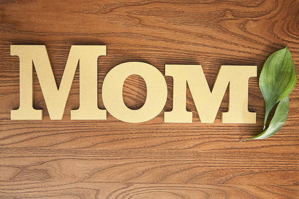 top view of green leaves and mom lettering on wooden surface - Foto, afbeelding