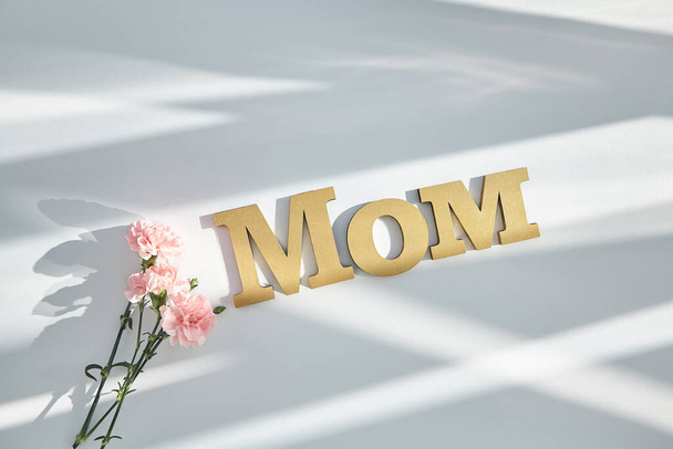 top view of pink carnations and mom lettering on white background with sunlight and shadows - Photo, Image