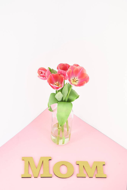 spring tulips in vase near mom lettering on pink and white background - Fotó, kép