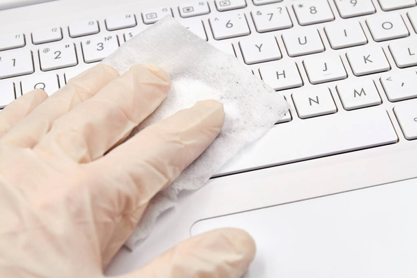 Az emberi kéz fehér védőkesztyűben fertőtlenítő kendő notebook felülettel tisztítja a koronavírus, baktériumok, vírusok és baktériumok megelőzésére. Közelkép, szelektív fókusz - Fotó, kép
