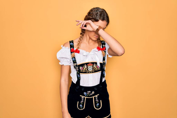Young beautiful blonde german woman with blue eyes wearing traditional octoberfest dress covering eyes with arm, looking serious and sad. Sightless, hiding and rejection concept - Photo, Image