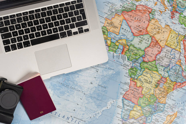 Προετοιμασία ταξιδιού με laptop και διαβατήριο σε παγκόσμιο χάρτη. - Φωτογραφία, εικόνα