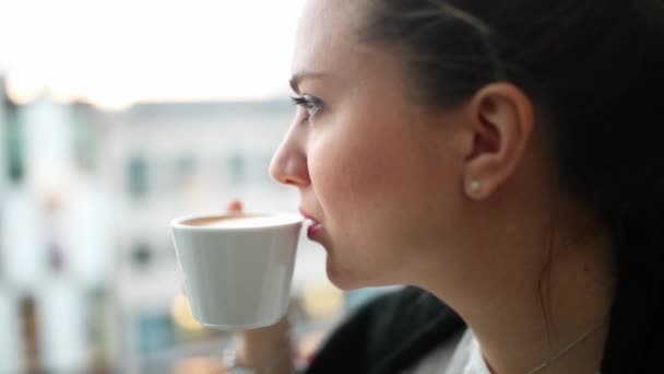 Beautiful blonde drinks coffee in a cafe and looks into the distance - Imágenes, Vídeo