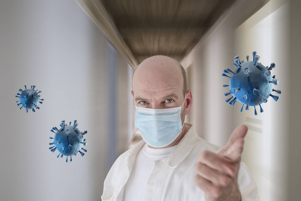 Egy védő maszkot viselő kaukázusi orvos a kórházi folyosón lévő Corona vírusra mutat.. - Fotó, kép