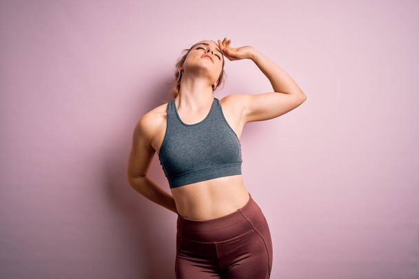 Young beautiful blonde sportswoman doing sport wearing sportswear over pink background stretching back, tired and relaxed, sleepy and yawning for early morning - Zdjęcie, obraz