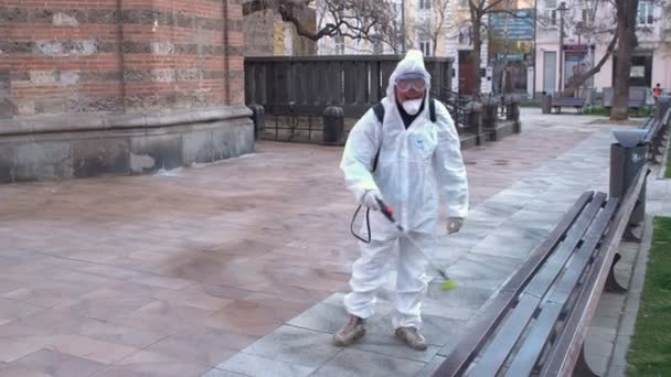 Sofia, Bulgaria - 11 April, 2020: Worker sprays disinfectant outside Sveti Sedmochislenitsi (Seven Saints) church against the spread of coronavirus disease COVID-19. - Filmagem, Vídeo