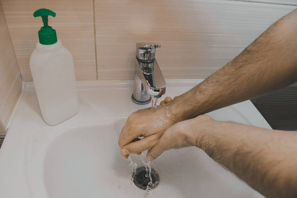 Mężczyzna myje ręce mydłem pod bieżącą wodą w łazience w domu.. - Zdjęcie, obraz