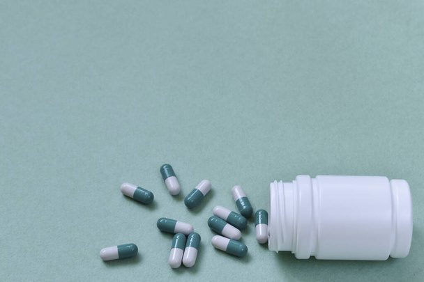 Dietary supplements. A few long capsules with tablets in front of an open bottle with no lid on a green background. Cover and antivirus protection. - Zdjęcie, obraz