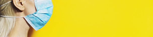 Chica joven que usa mascarilla respiratoria médica contra el coronavirus. Retrato panorámico sobre fondo amarillo con espacio para copiar
. - Foto, imagen