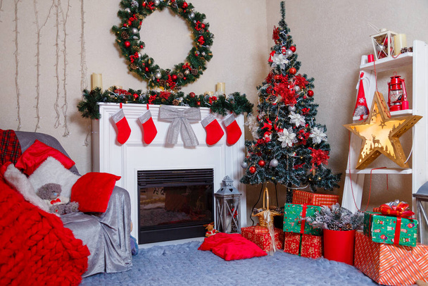 Feliz Navidad salón interior con abeto decorado, chimenea, corona, estrella, conos, bombillas, cajas de regalo y cuadros rojos en el sillón. Concepto de vacaciones de Año Nuevo e invierno
.  - Foto, imagen