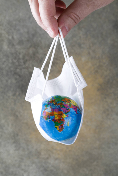 Human hand holds earth lying in medical mask on grey background. Save planet from corona virus. reduce risk of infection and spreading the virus. - Fotografie, Obrázek