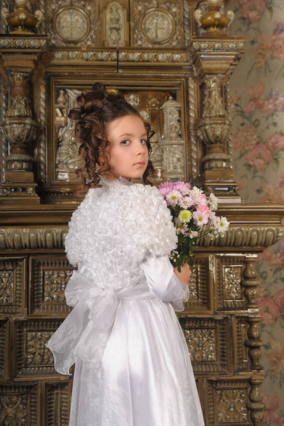 child girl in a white dress with a hairstyle in retro style with flowers in her hands - Photo, Image