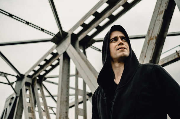 Brutal man in a hood on a background of metal structures - 写真・画像
