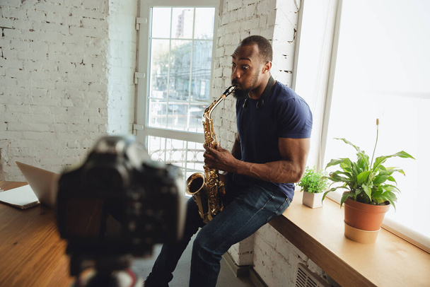 Afrikai-amerikai zenész szaxofonozik online koncert során otthon elszigetelt és karantén alá helyezett, lenyűgöző improvizáció - Fotó, kép