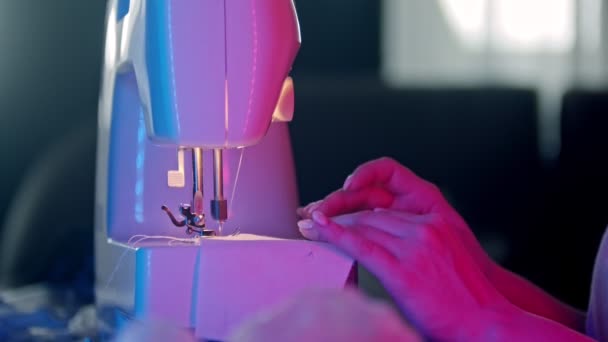 Руки молодой женщины швеи с аккуратными ногтями шитья белой тканью с помощью швейной машинки в неоновом освещении
 - Кадры, видео