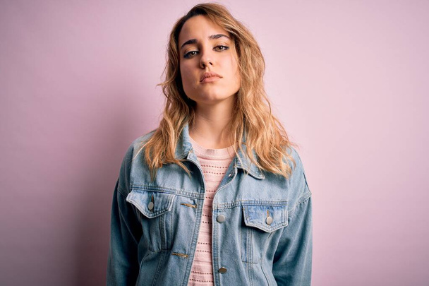 Young beautiful blonde woman wearing casual denim jacket standing over pink background Relaxed with serious expression on face. Simple and natural looking at the camera. - Фото, изображение