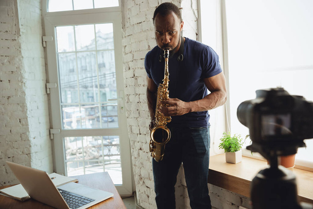 African-american musician playing saxophone during online concert at home isolated and quarantined, improvising on camera - Photo, Image
