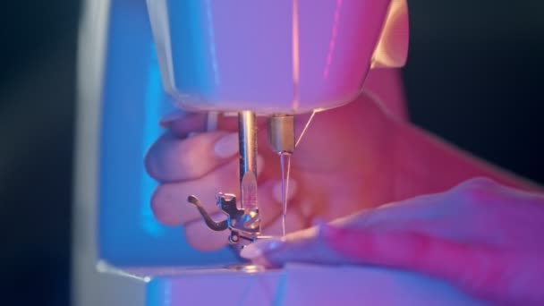 Руки швеи, шьющие белую ткань с помощью швейной машинки при неоновом освещении
 - Кадры, видео
